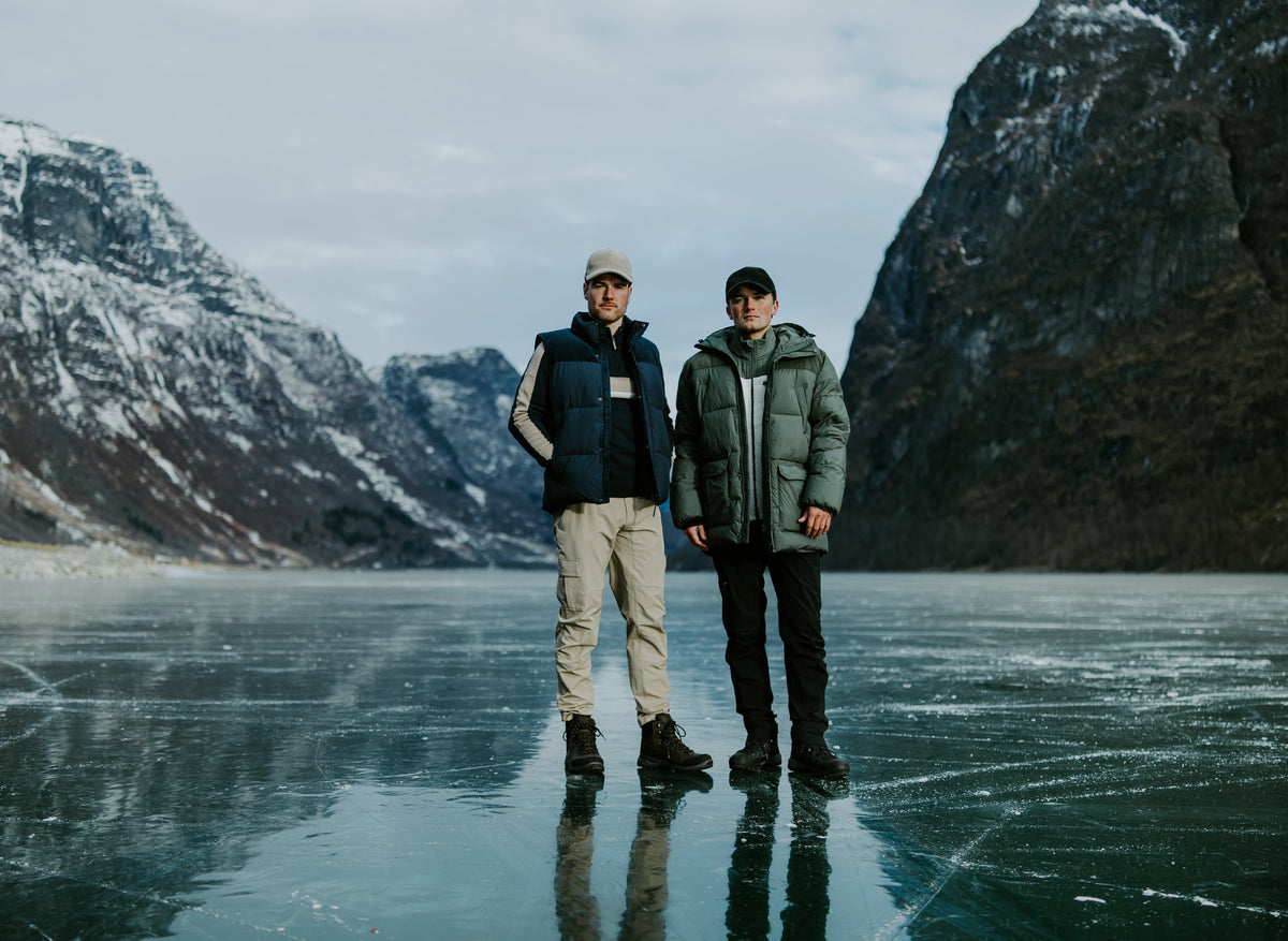 To menn i vinterjakker på frossen fjord med bratte fjell bak