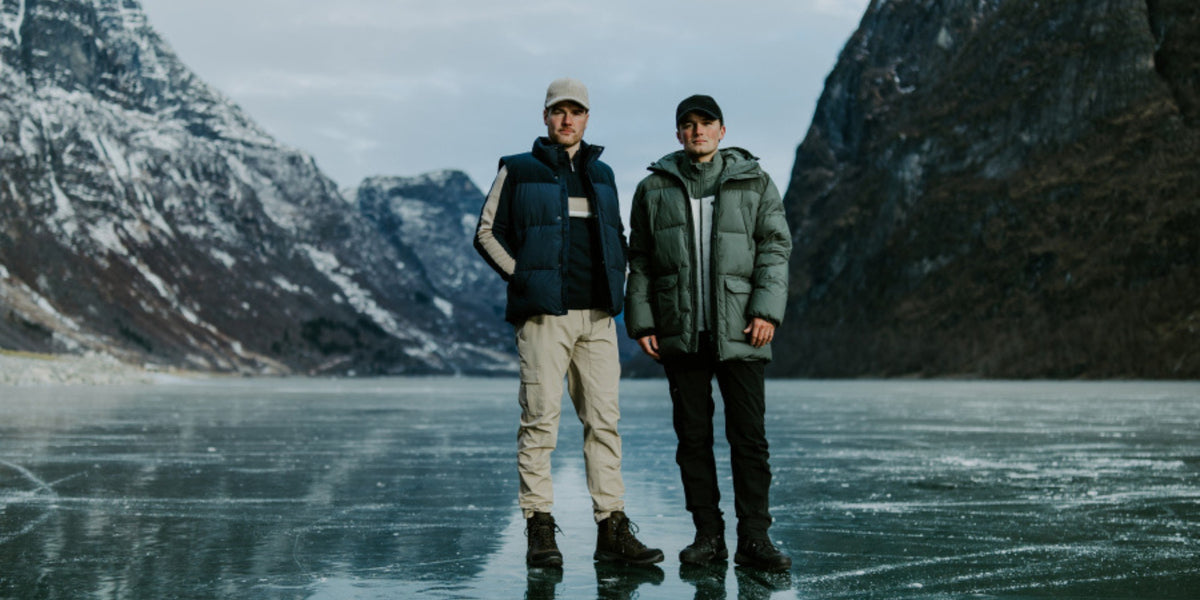 To menn i vinterjakker på frossen fjord med bratte fjell bak